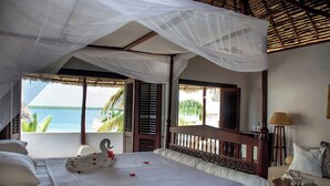 A bedroom with a bed, a canopy, a view of the sea, and a balcony with shutters.