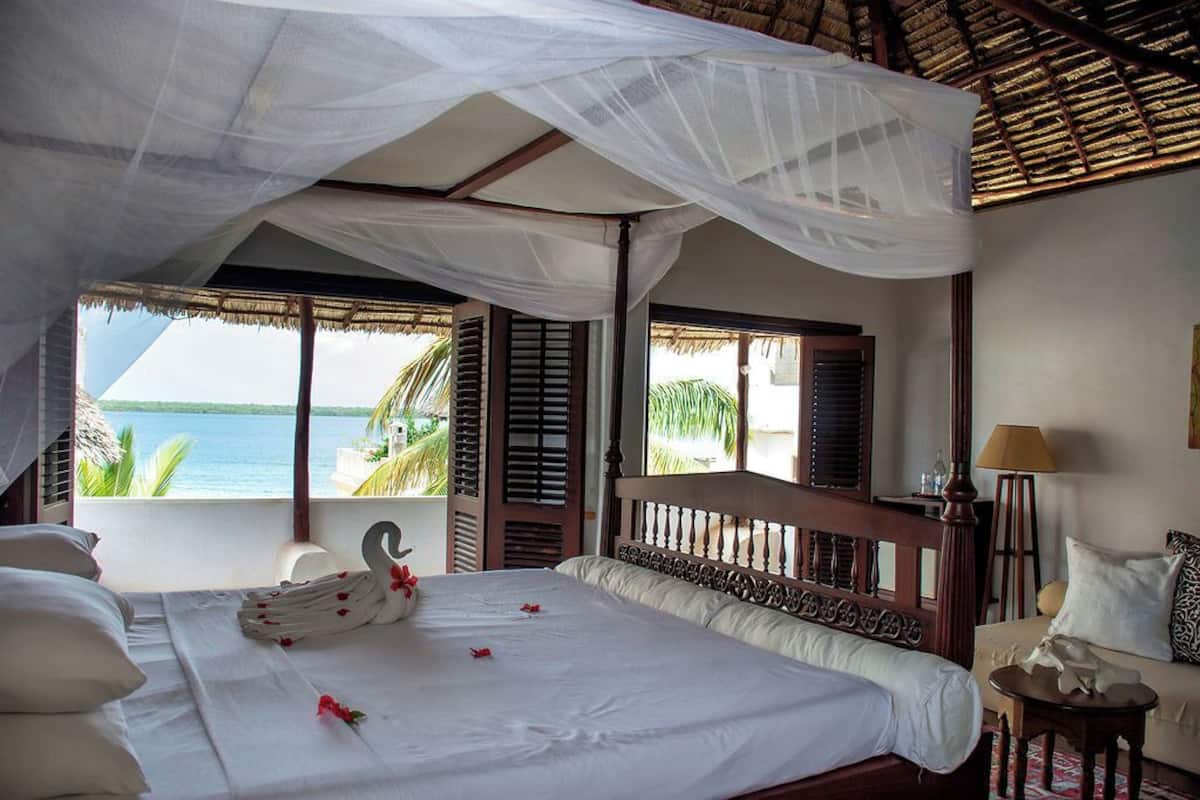 Ein Schlafzimmer mit Bett, Baldachin, Meerblick und einem Balkon mit Fensterläden.