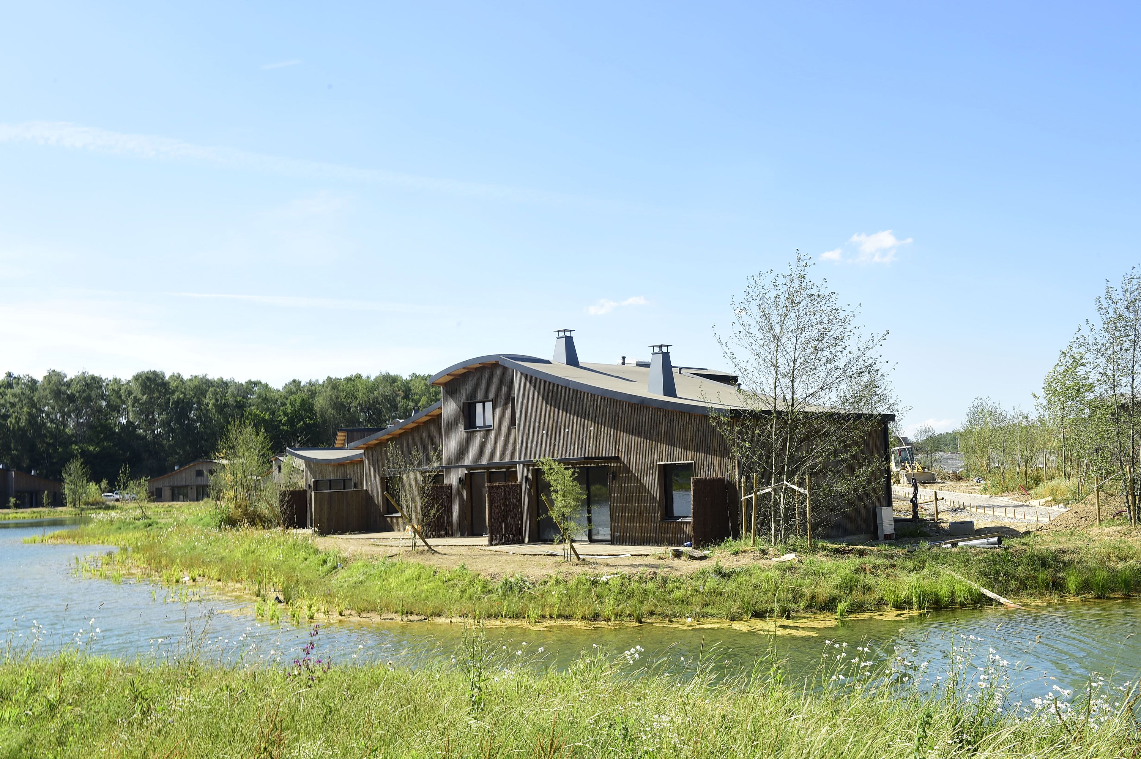 A modern house with a large garage and a covered outdoor area, situated by a calm body of water.