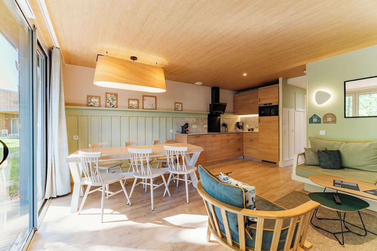 A modern kitchen with wooden cabinets, a dining area with white chairs, and a cozy seating area with a green sofa and a small table.