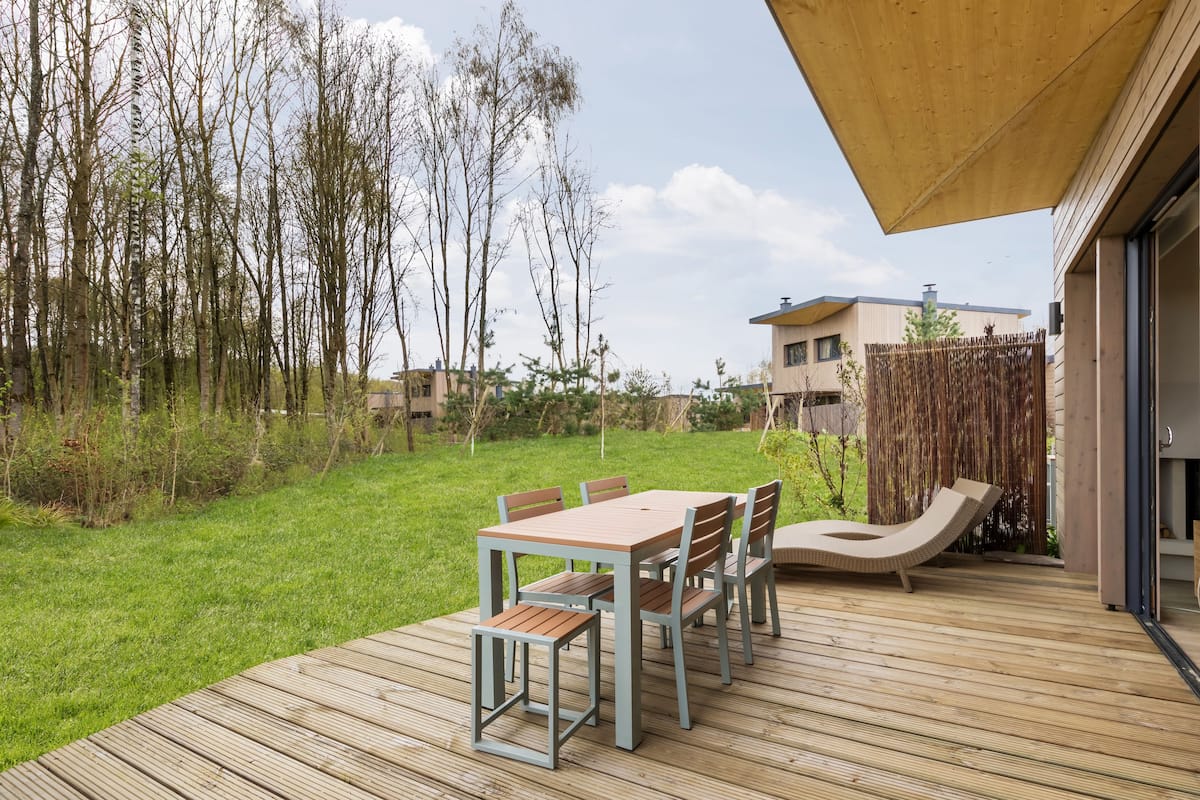 A deck with a table and chairs, a lounge chair, and a wooden fence.