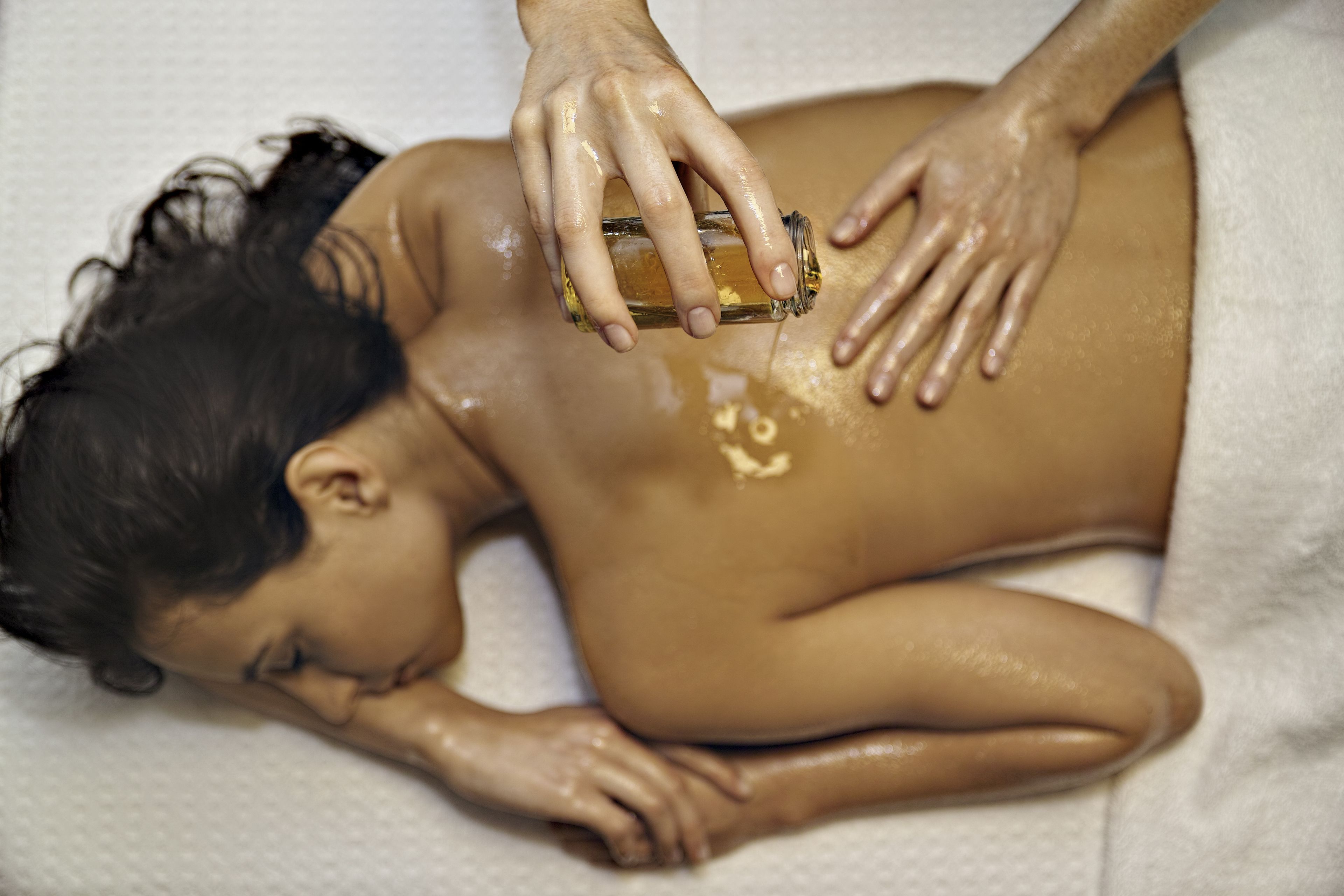 A person receiving a massage with a bottle of oil being applied to their back.