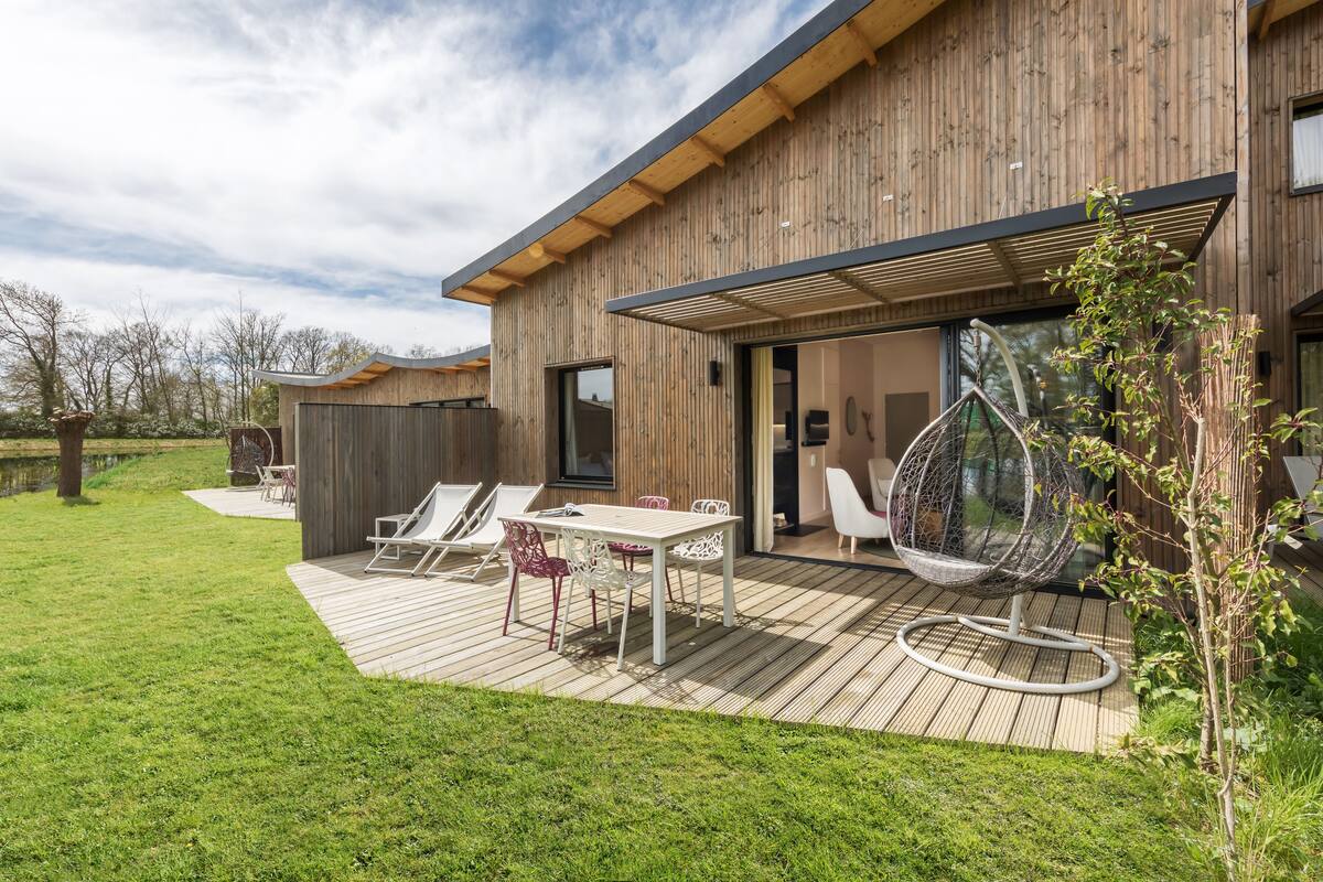 A modern house with a wooden exterior, a deck with outdoor furniture, and a hanging chair.