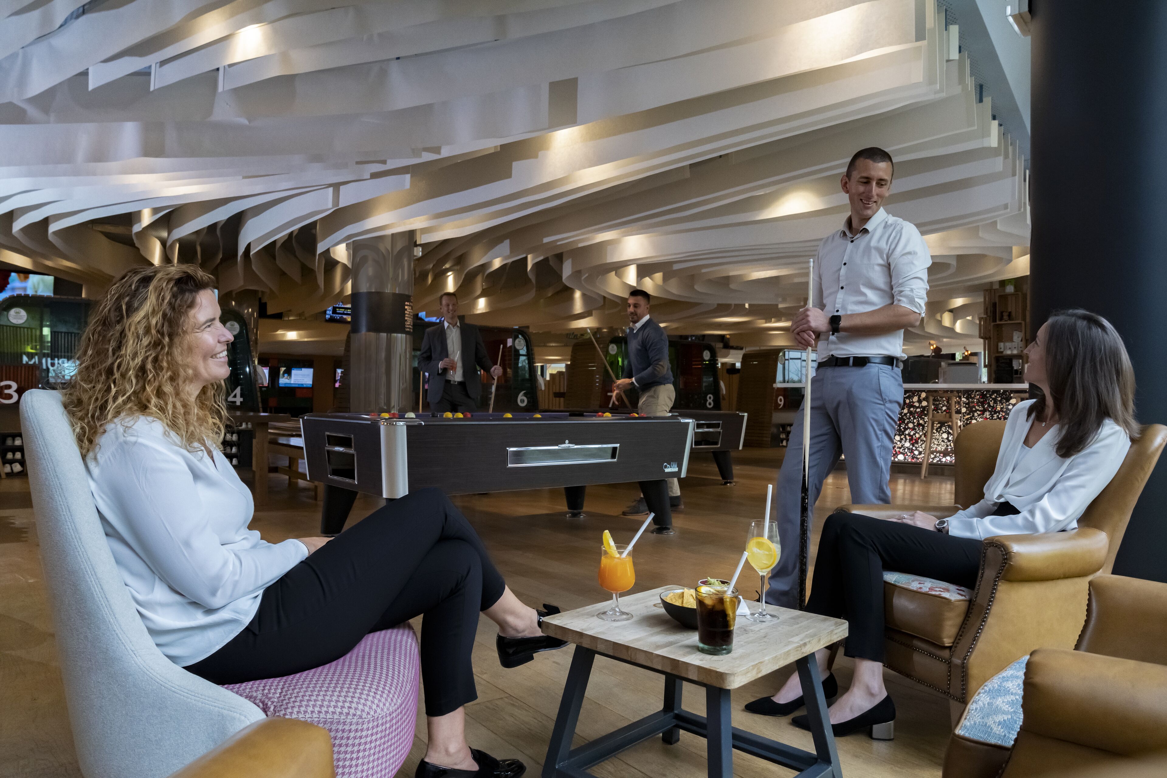 A modern lobby with a pool table, seating areas, and a bar.