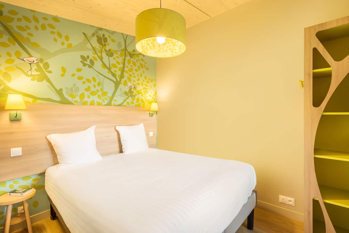 A modern hotel room with a large bed, a wooden headboard, a wall mural, and a unique shelving unit.