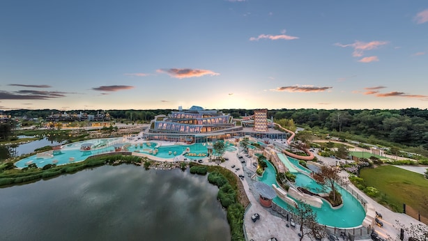 A resort with multiple swimming pools, a large building with a glass facade, and a surrounding natural landscape. - Center Parcs Villages Nature Paris (Villeneuve-le-Comte)