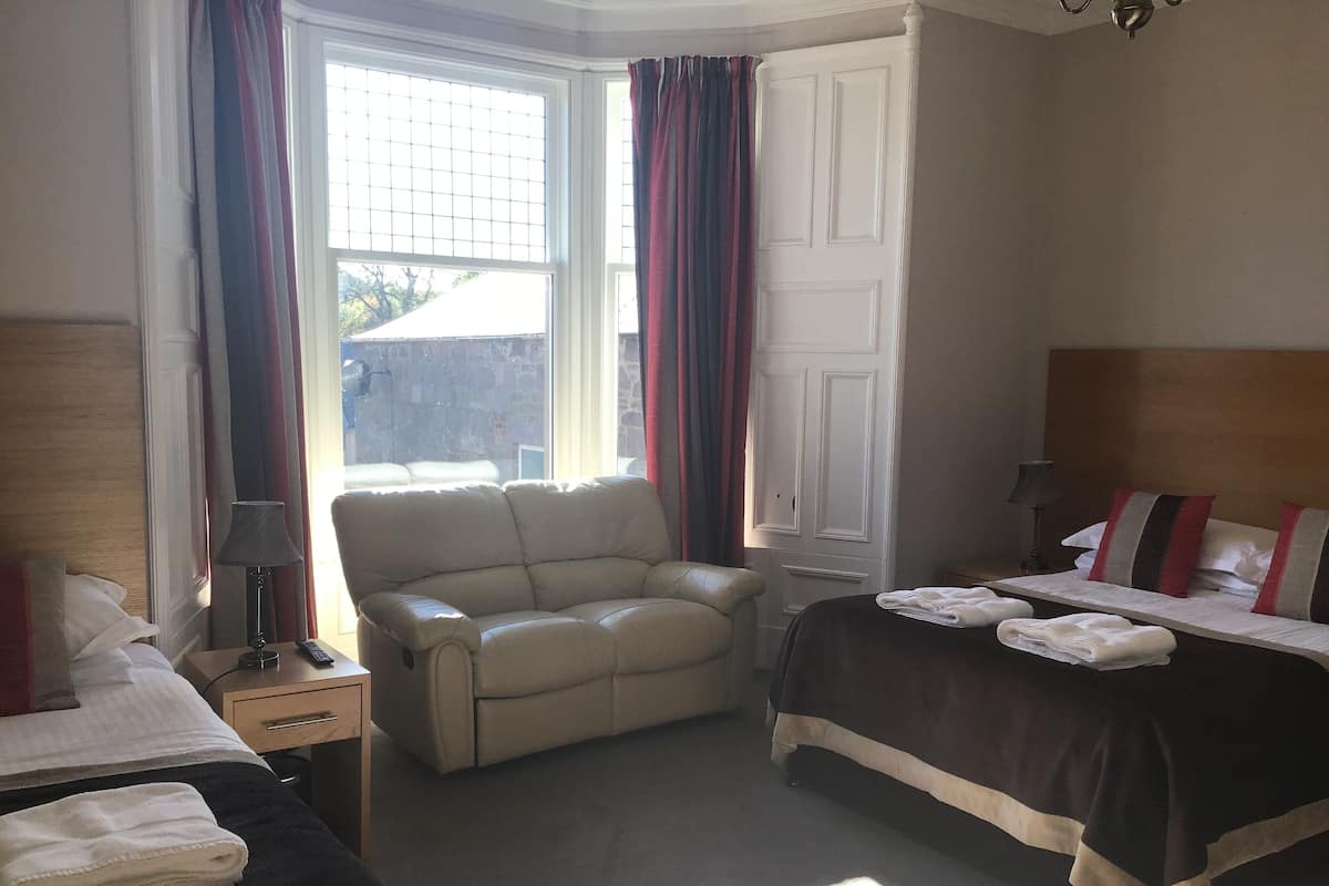A hotel room with a bed, a chair, a desk, and a window with curtains.