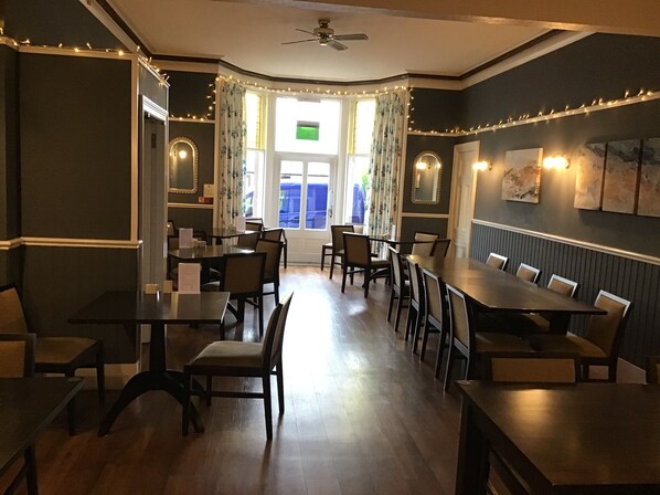 A restaurant with multiple tables and chairs, a ceiling fan, and string lights.