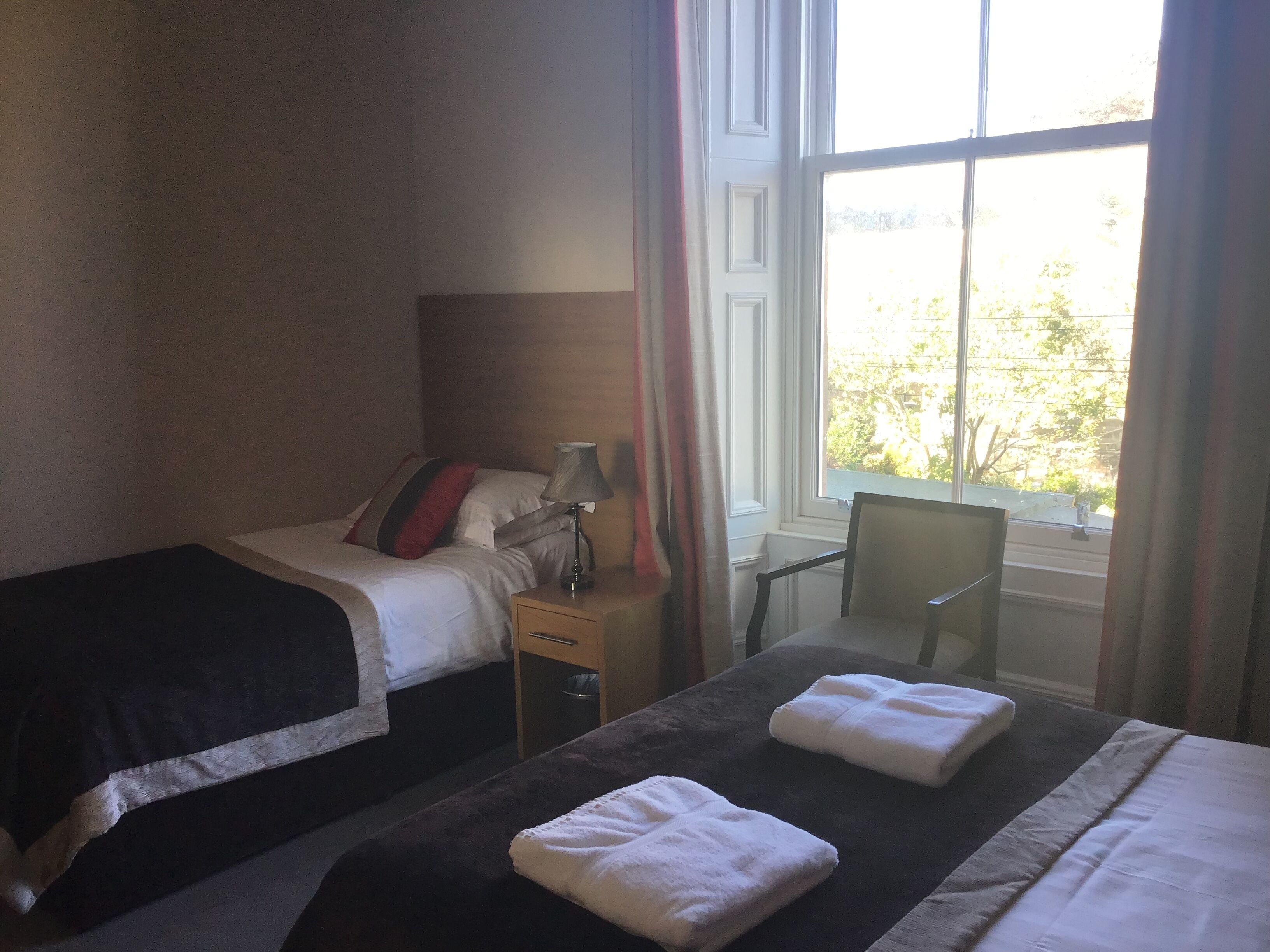 Habitación de hotel con dos camas, una mesita, una silla y una ventana con cortinas.