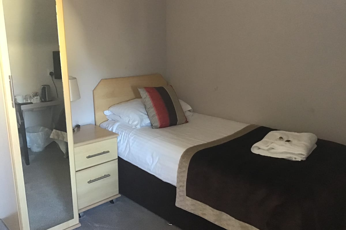 A hotel room with a bed, a bedside table, a mirror, and a small desk.