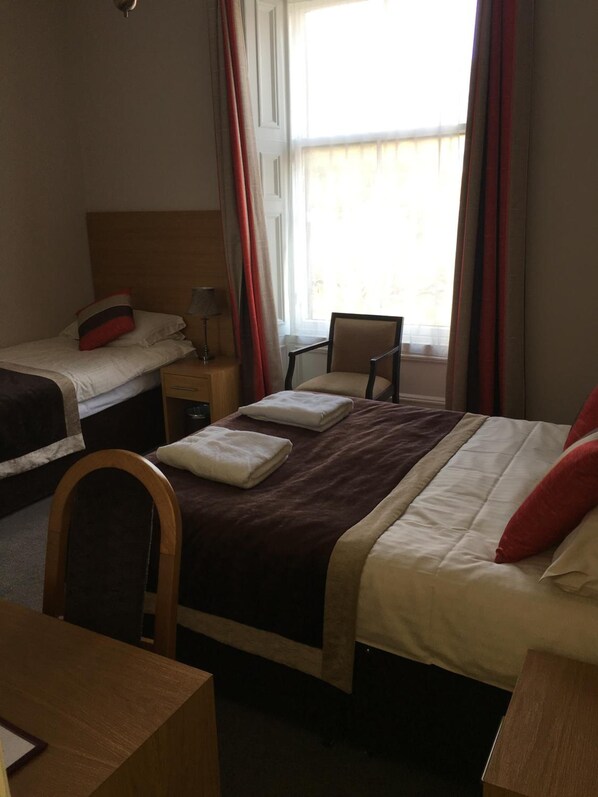 A hotel room with two single beds, a wooden chair, a desk, and a window with curtains.