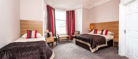 A hotel room with two beds, a desk, a chair, a chandelier, and a window with curtains.