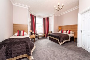 A hotel room with two beds, a desk, a chair, a chandelier, and a window with curtains.