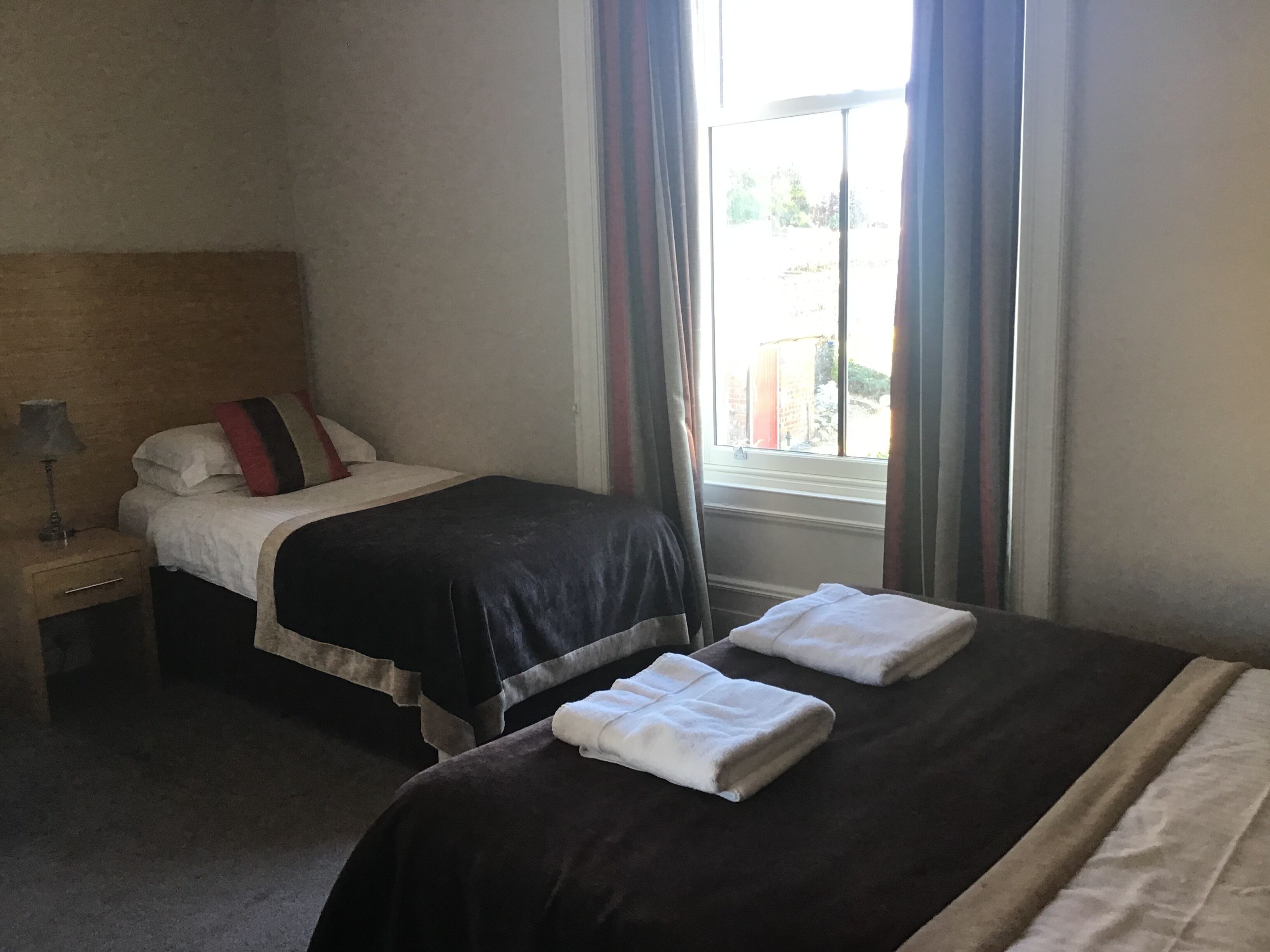 Une chambre d’hôtel avec deux lits, une table de chevet, une lampe et une fenêtre avec des rideaux.