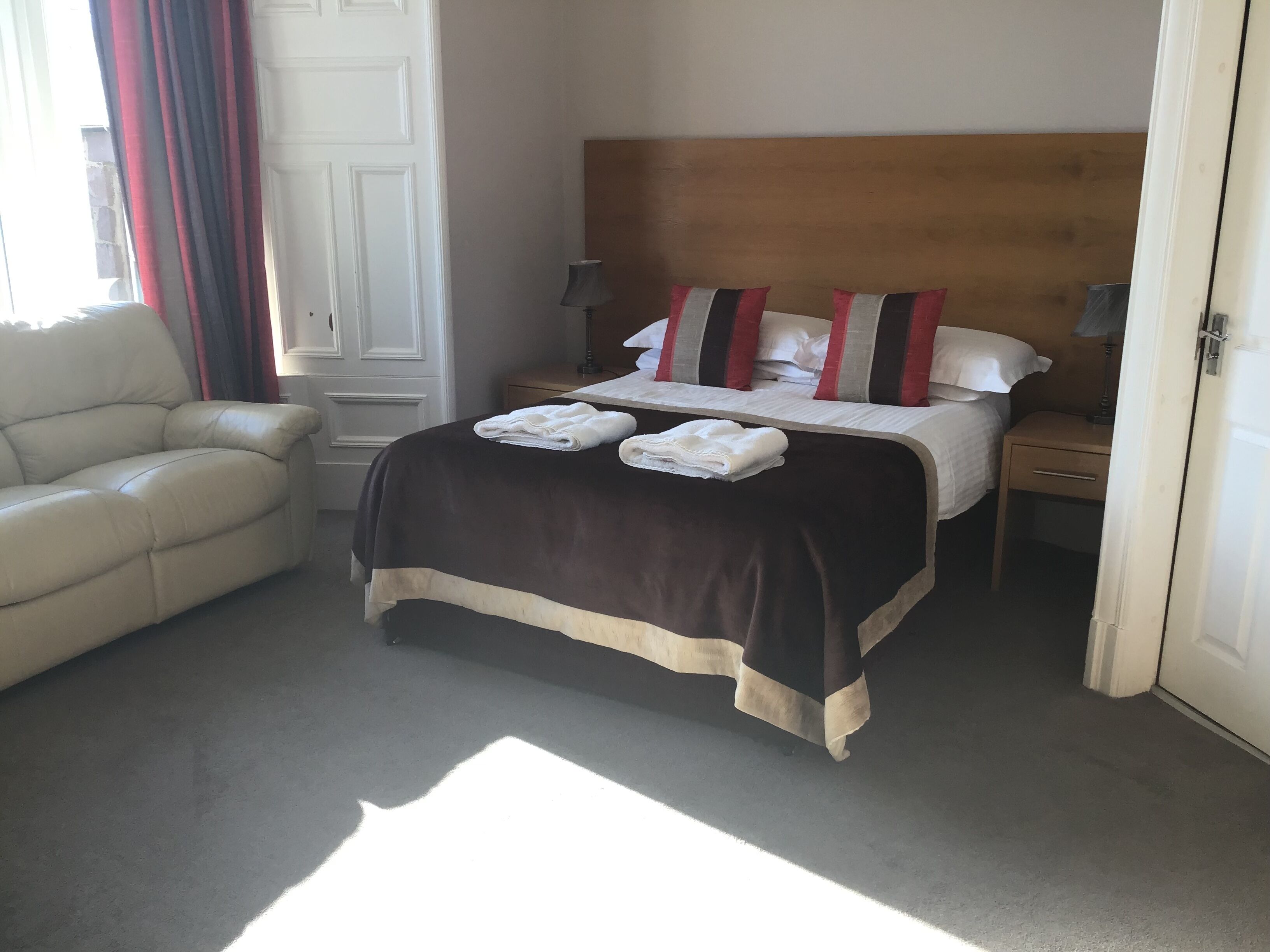 A hotel room with a bed, a nightstand, a lamp, a chair, and a door.