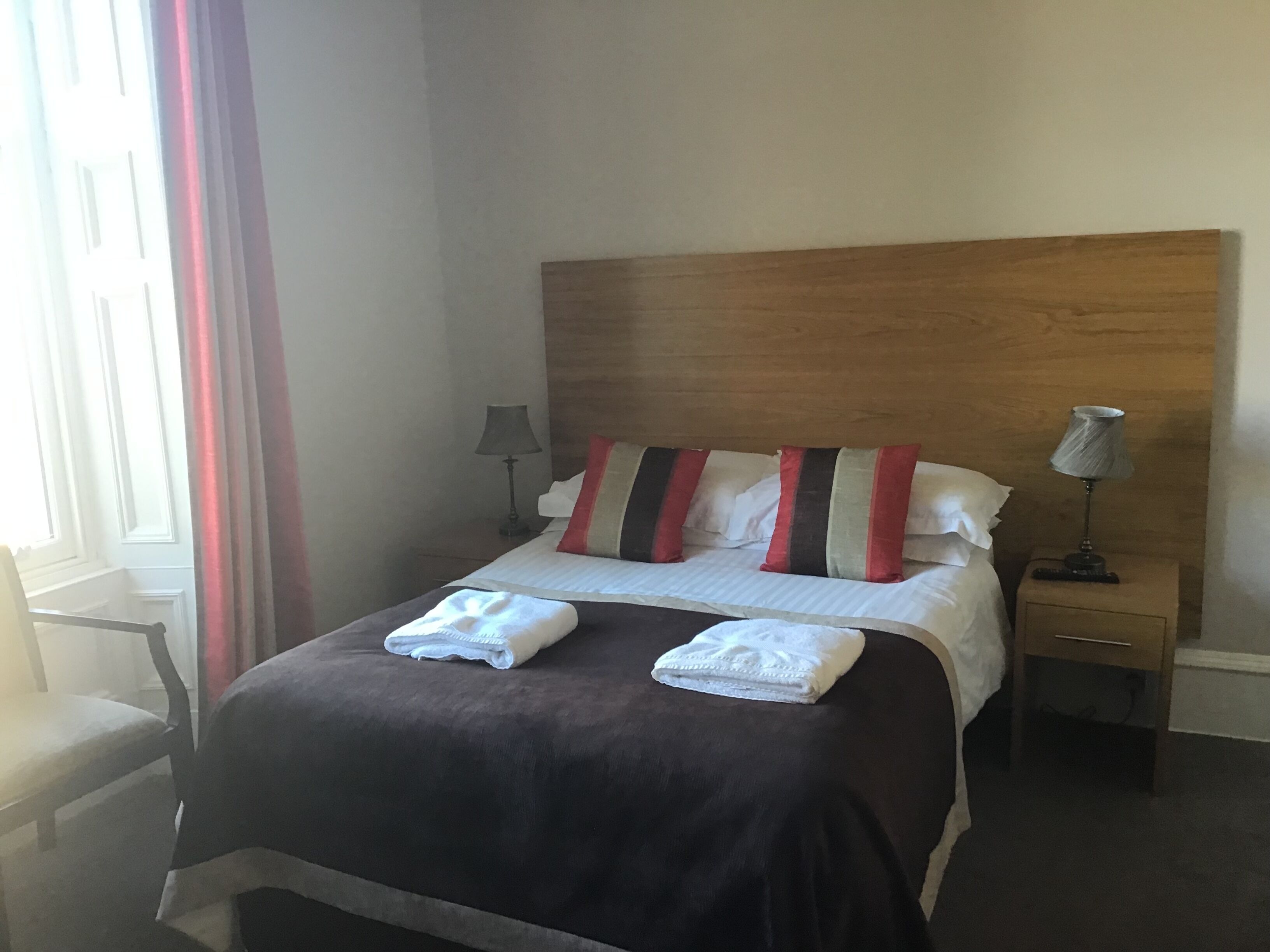 A neatly made bed with two white towels, a wooden headboard, and striped pillows.