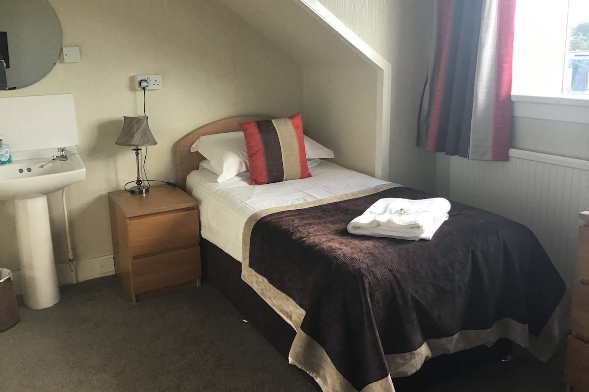 A bedroom with a bed, a bedside table, a lamp, a sink, and a mirror.