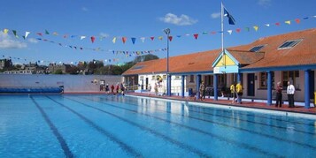 A swimming pool with clear lanes, a covered spectator area, and a building with a red roof.