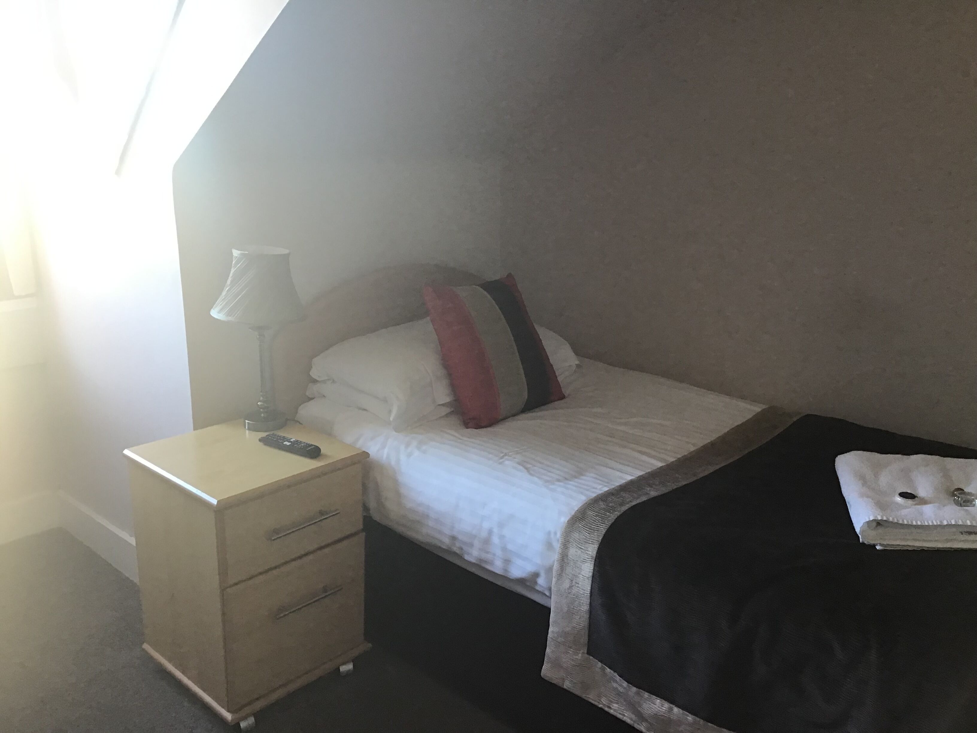 Una habitación de hotel con una cama, una mesita de noche con lámpara y un mueble bajo para guardar objetos.