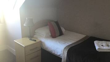Una habitación de hotel con una cama, una mesita de noche con lámpara y un mueble bajo para guardar objetos.