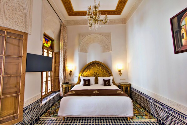 A hotel room with a large bed, ornate headboard, chandelier, and patterned floor. - Riad Marjana Suites & Spa (Fes)