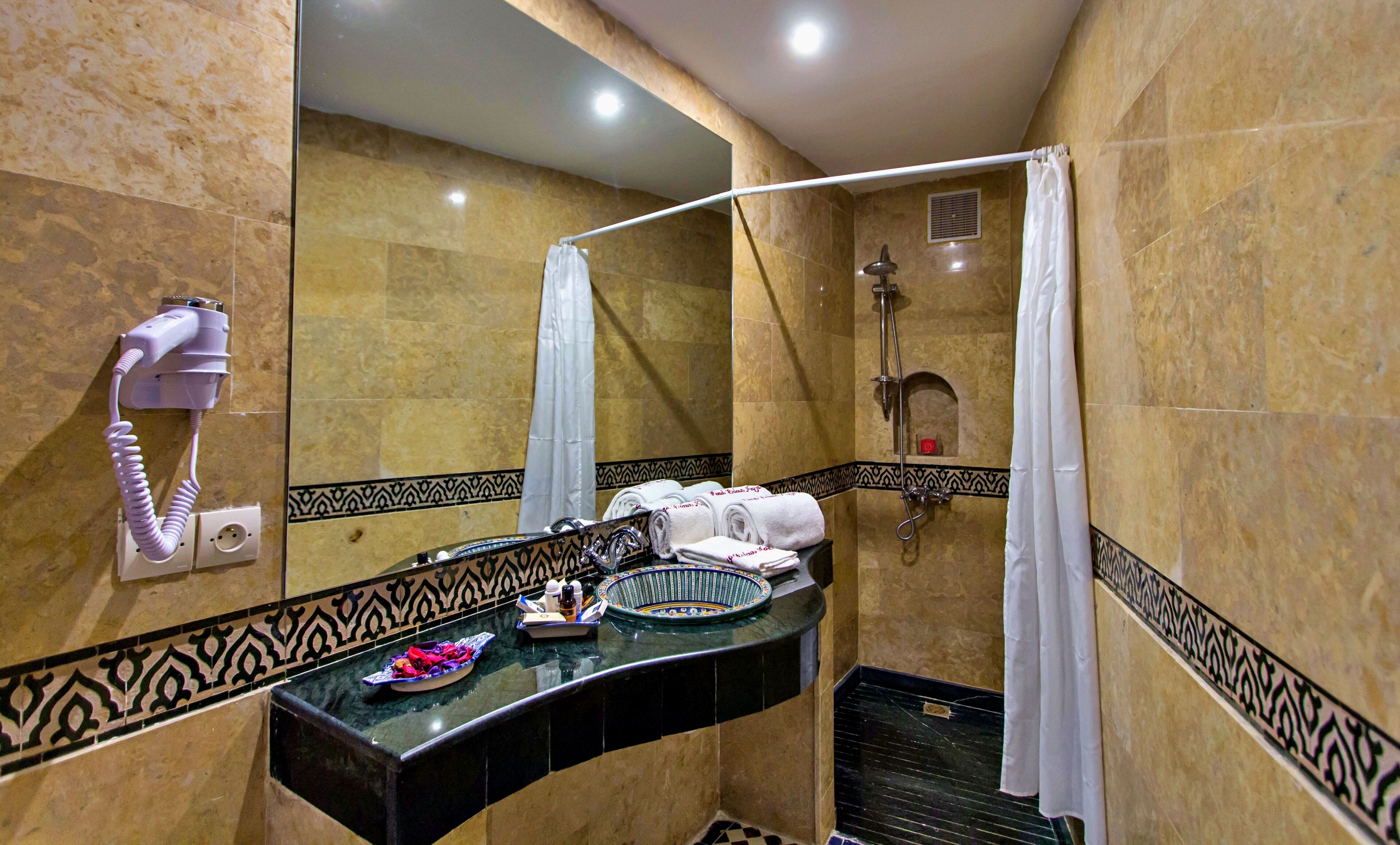 Casa de banho com chuveiro, secador de cabelo, porta-toalhas e lavatório com um prato decorativo.