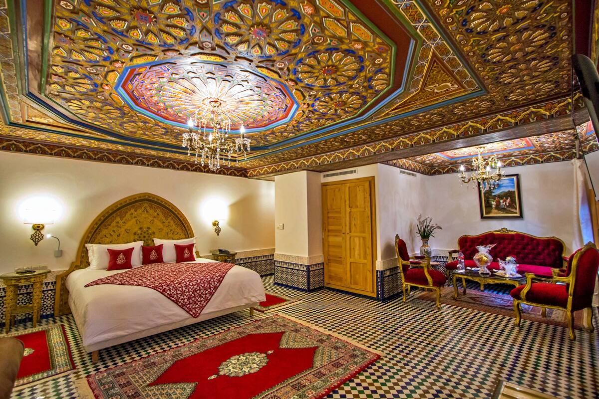 A room with a large bed, a red sofa, and a chandelier.