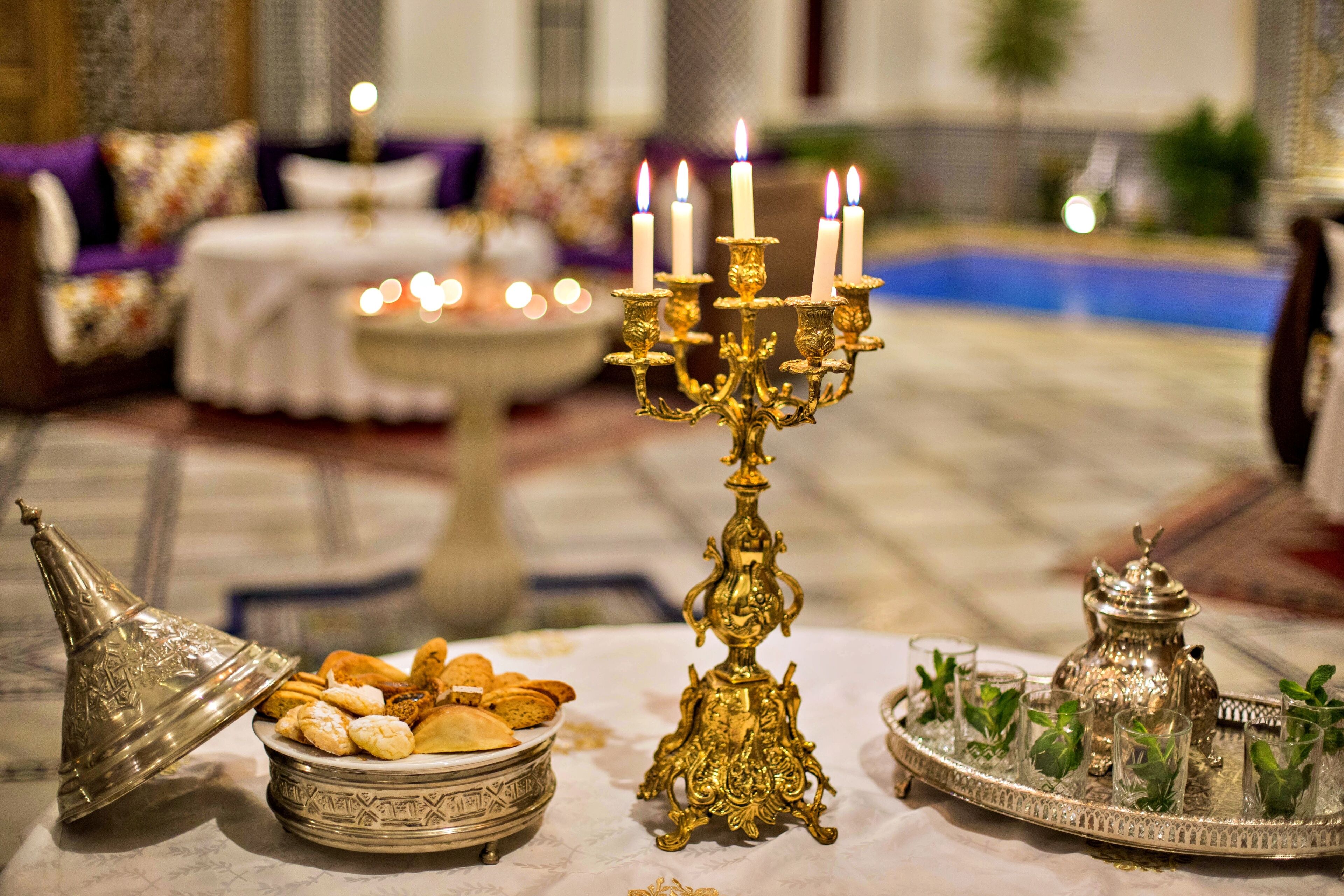 A table with a decorative candelabra, a silver tray with glasses, and a silver container with pastries.