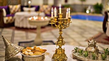 A table with a decorative candelabra, a silver tray with glasses, and a silver container with pastries.