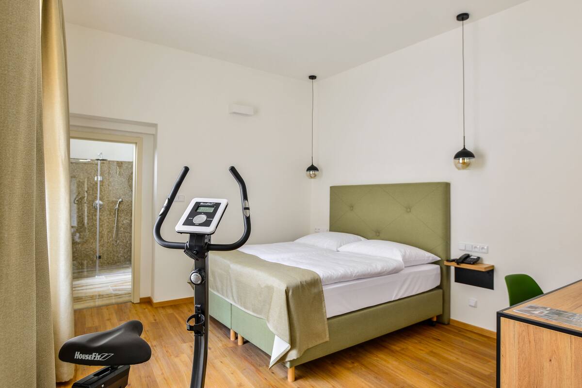 A bedroom with a bed, exercise bike, and a shower area.