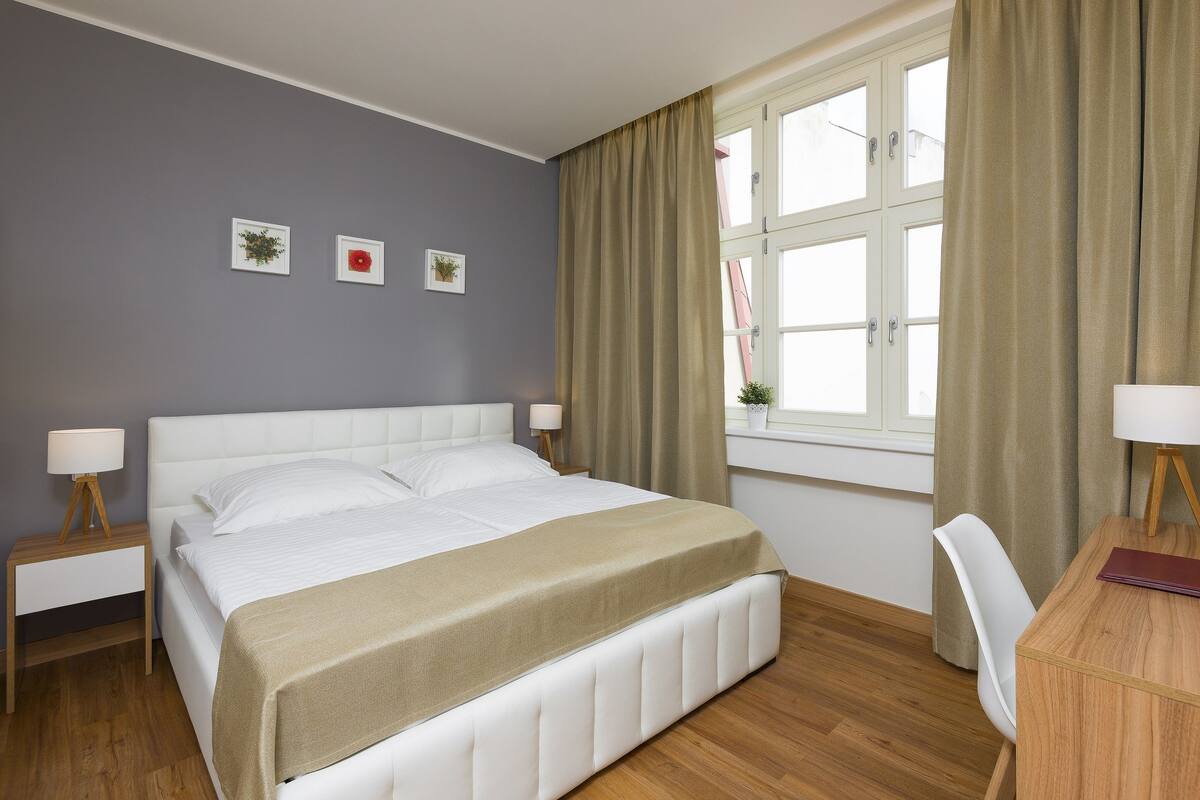 A neatly arranged hotel room with a large bed, bedside tables with lamps, a small desk, and a window with curtains.