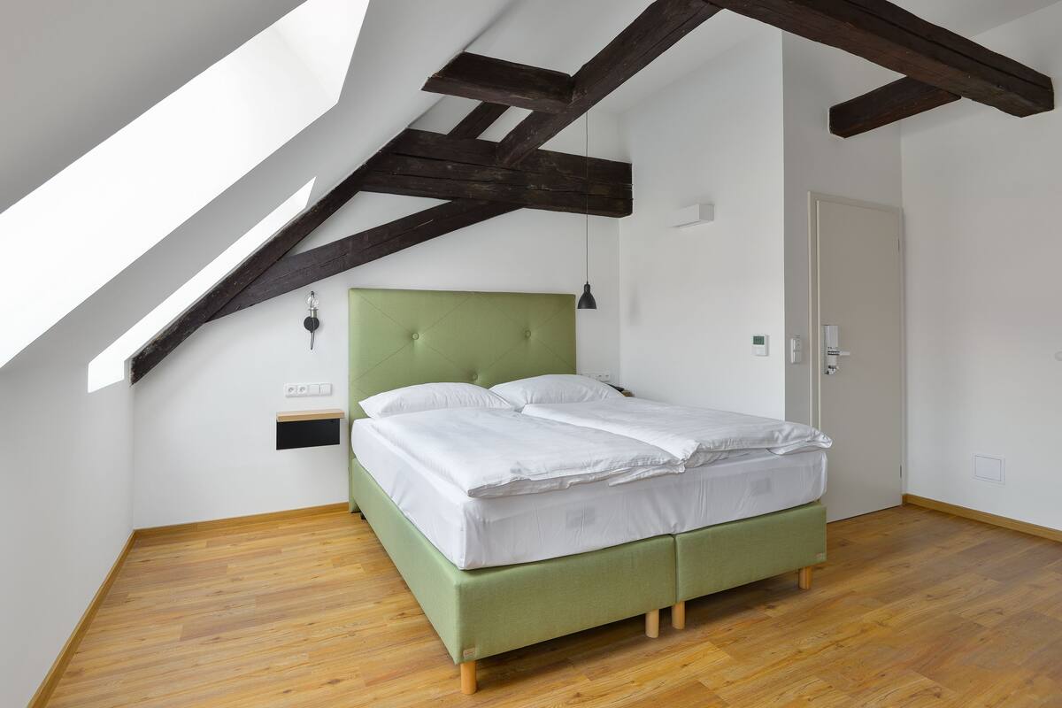 A room with a green bed, wooden beams, a sloped ceiling, and a wooden floor.