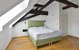 Quarto com cama, vigas de madeira, claraboia e porta.