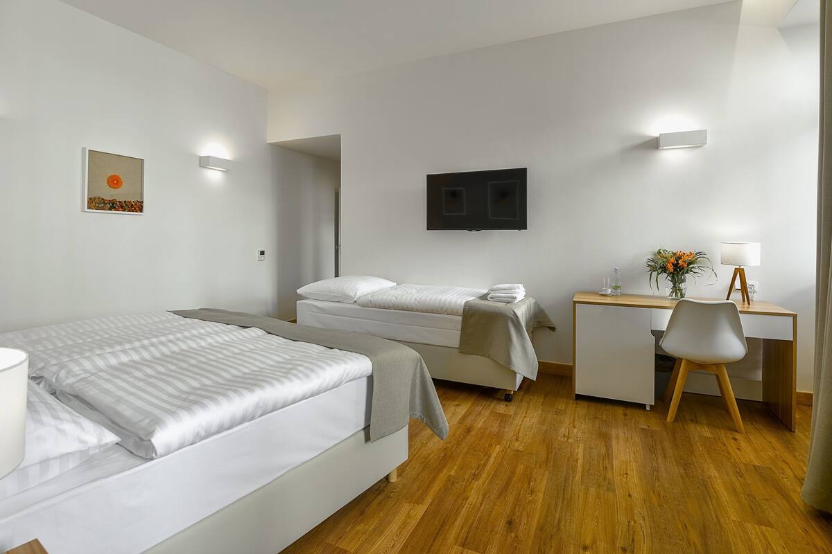 A hotel room with two beds, a desk, a chair, a TV, and a painting on the wall.