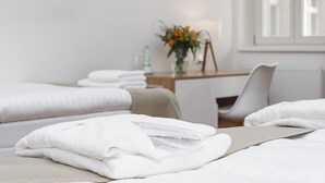A hotel room with two beds, a desk, and a chair. There is a vase with flowers on the desk. - Hotel Garden Court (Prague)