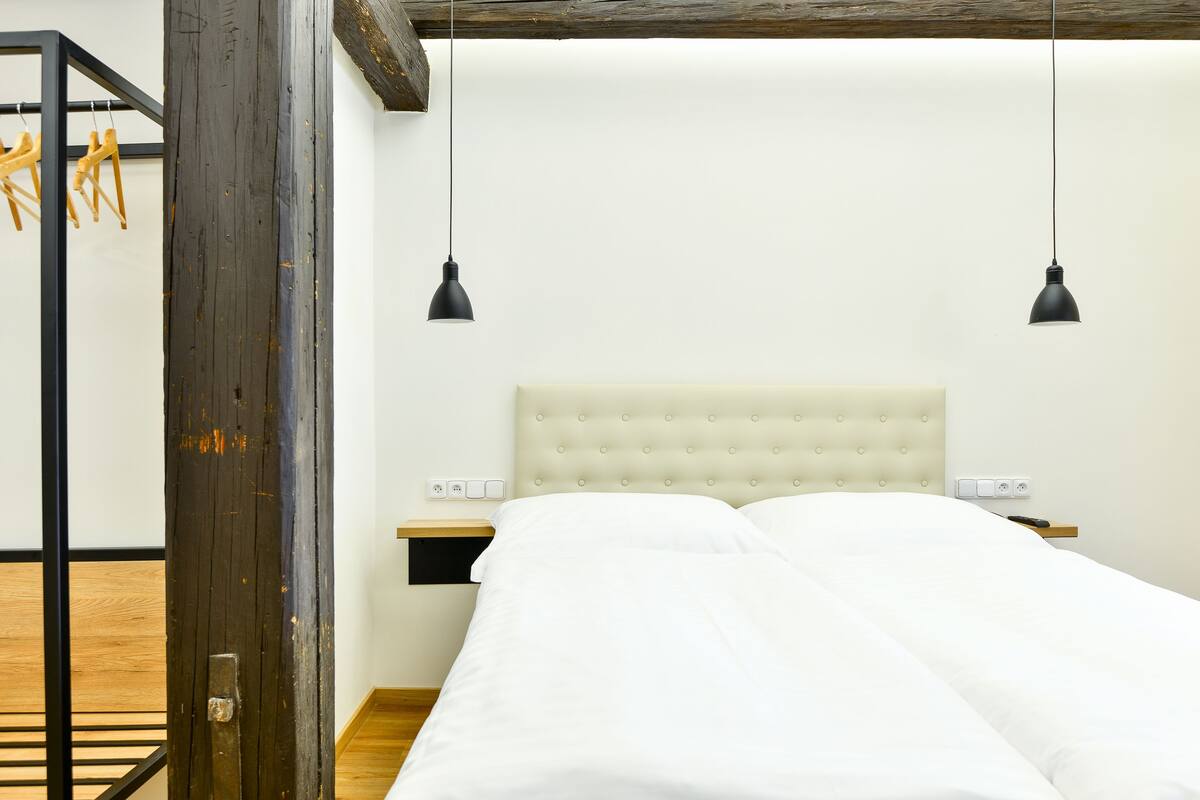 A bedroom with a white bed, two bedside tables, and two hanging pendant lights.