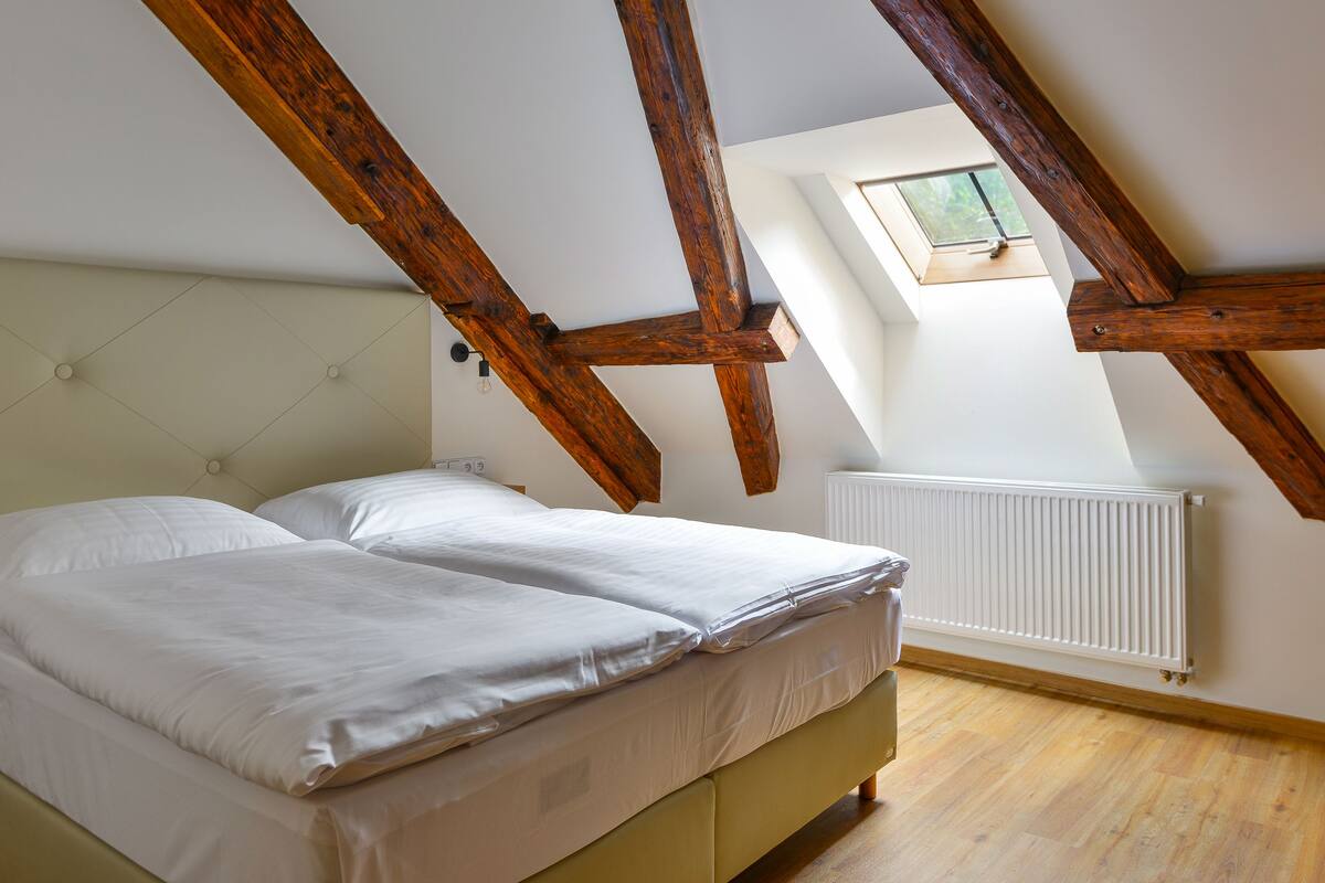 A bedroom with a bed, wooden beams, a window, and a radiator.