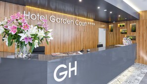 En hotelreception med en væg af træpaneler, en stor blomsterdekoration og et skilt med teksten Hotel Garden Court.