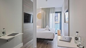 Una habitación de hotel moderna con una cama, una mesita de noche, una computadora portátil y una botella de agua.
