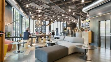 Un interior moderno con una zona de estar central, una recepción y amplias ventanas que dejan entrar luz natural.