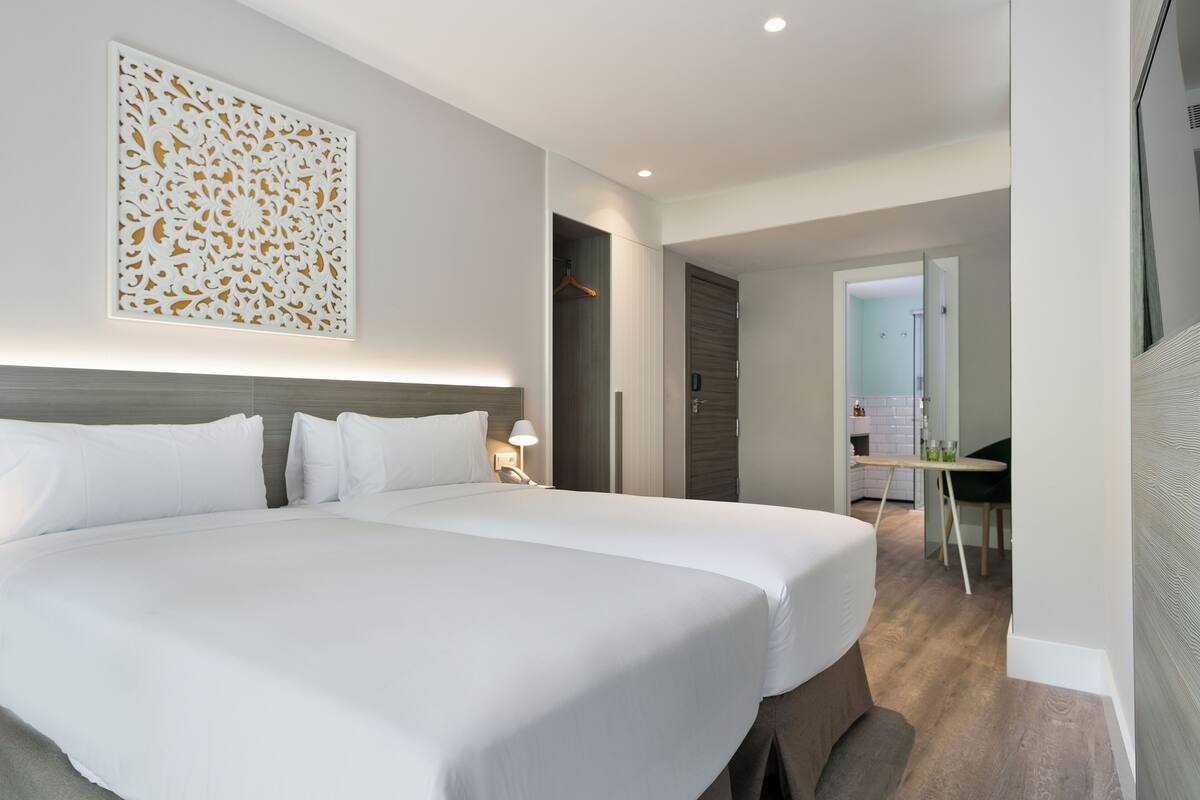 A hotel room with two beds, a decorative wall panel, a desk, and a walk-in closet.