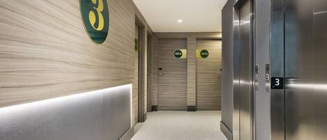 A modern elevator area with a number 3 sign on the wall, two elevators, and a corridor with a light-colored floor.