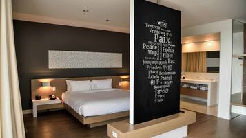 Een moderne hotelkamer met een groot bed, nachtkastjes, een kunstwerk aan de muur en een badkamer met wastafel en spiegel.