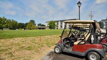 A golf cart parked on a sandy area with a building in the background.