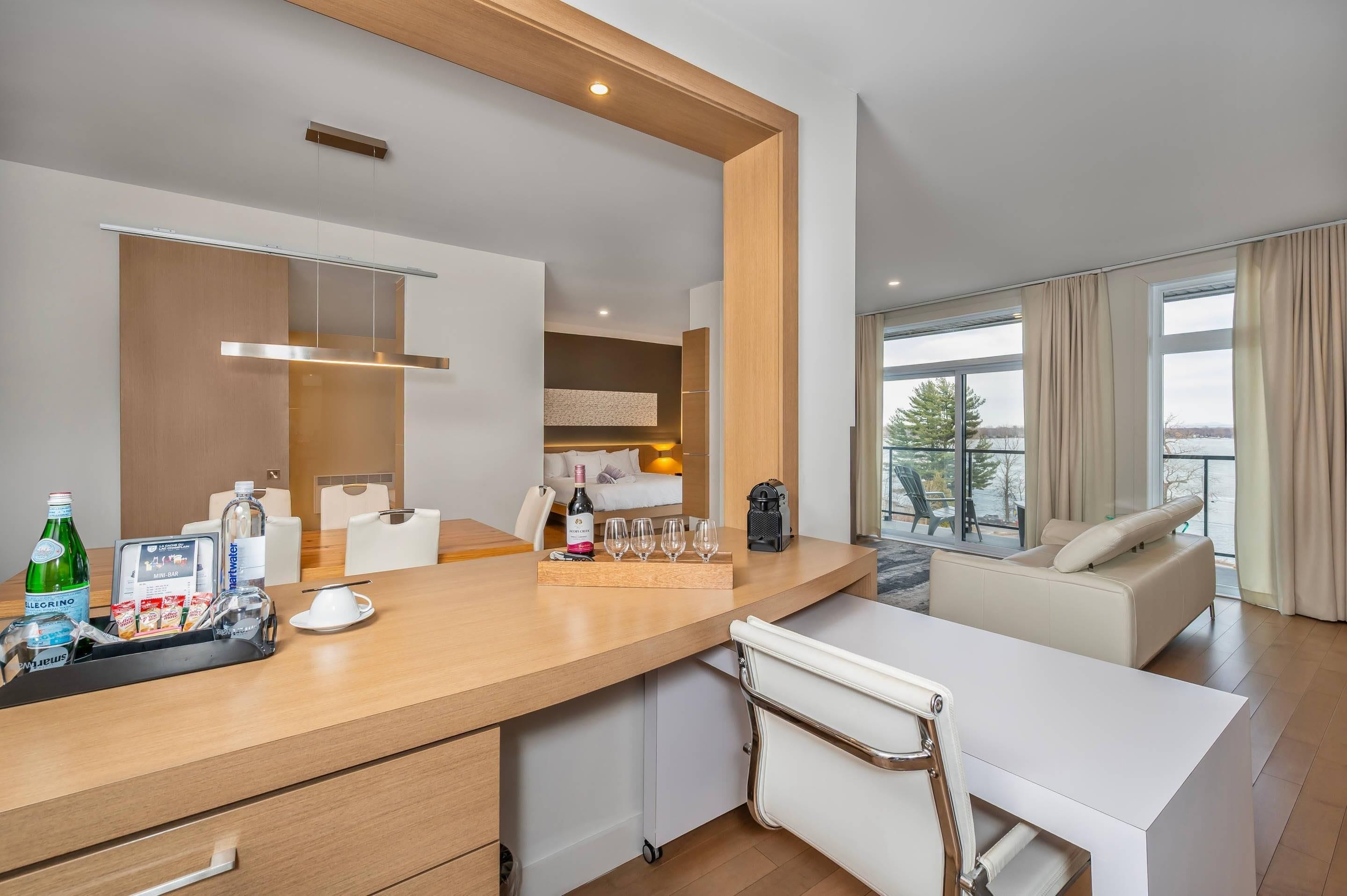 Una habitación de hotel moderna con zona de comedor, minibar y balcón con vistas.