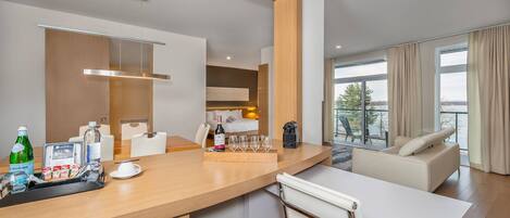 Una habitación de hotel moderna con zona de comedor, minibar y balcón con vistas.
