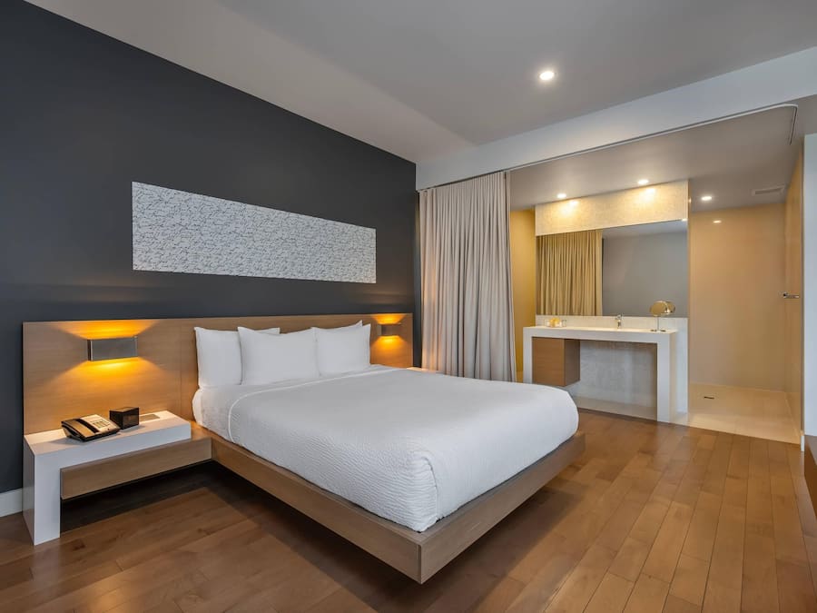 Een moderne hotelkamer met een groot bed, nachtkastjes, een bureau met spiegel en een badkamer die door een open deur zichtbaar is.