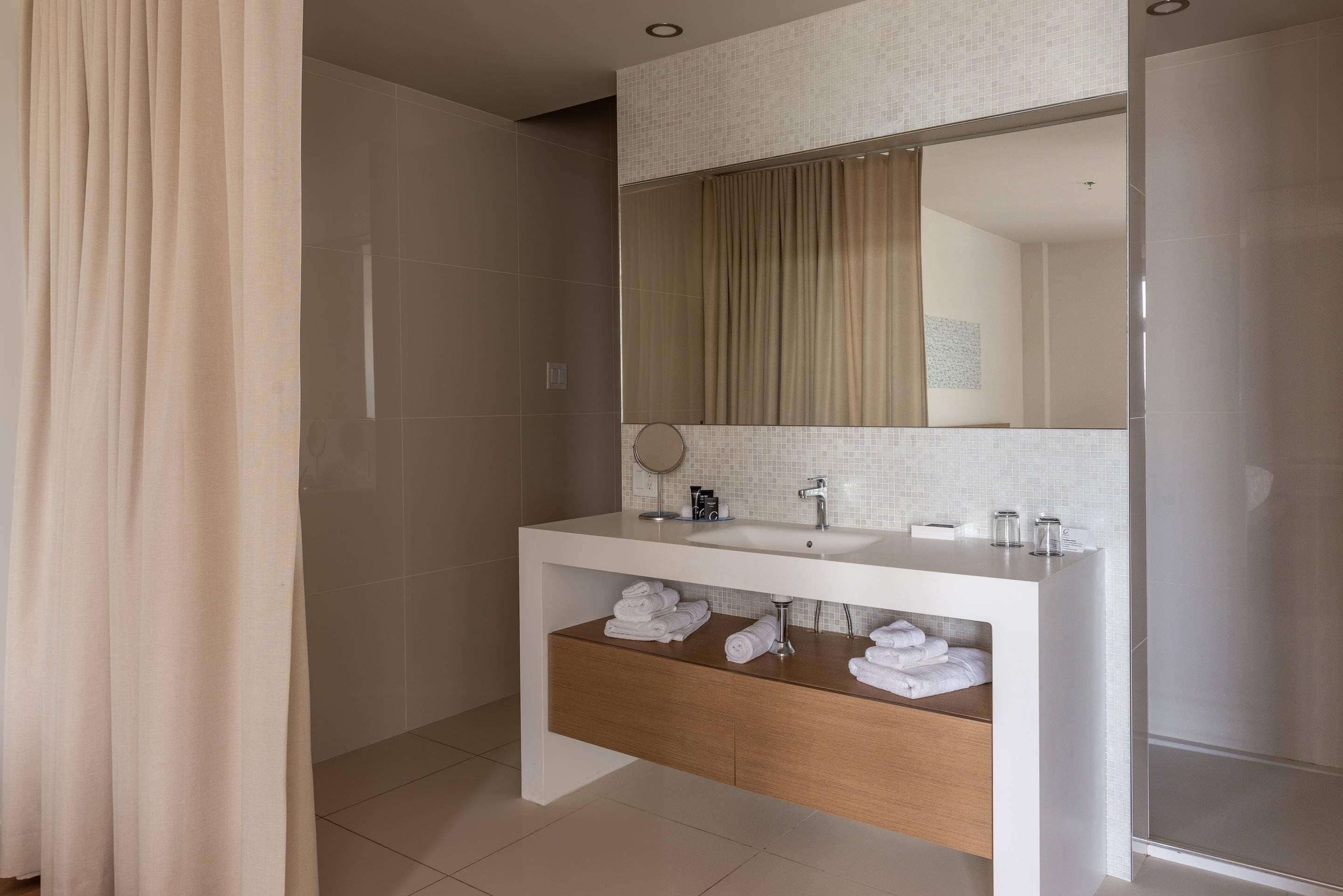 A modern bathroom with a white vanity, a mirror, and a shower area.