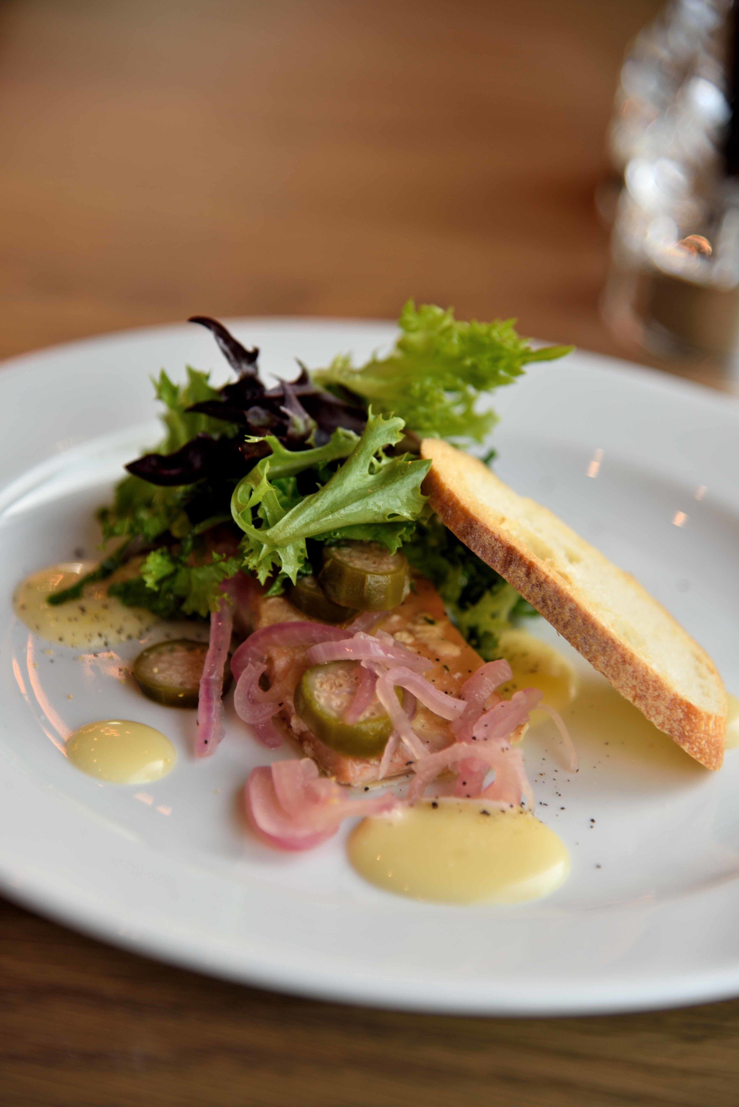 Une assiette blanche contenant une salade composée de légumes verts, d’oignons en tranches et d’un morceau de pain.