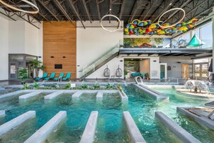 Una piscina interior con agua cristalina, rodeada de sillas de descanso y una pared de madera.